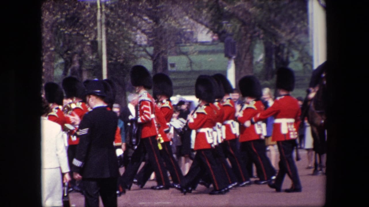 A line of guards in red uniforms marches beside spectators and officers.