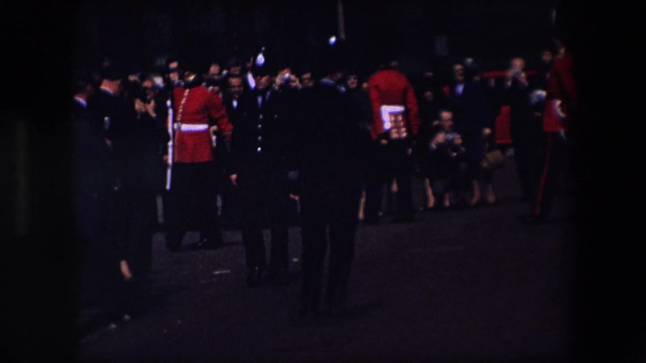 Crowd and uniformed guards gathered in a dark street-side view.