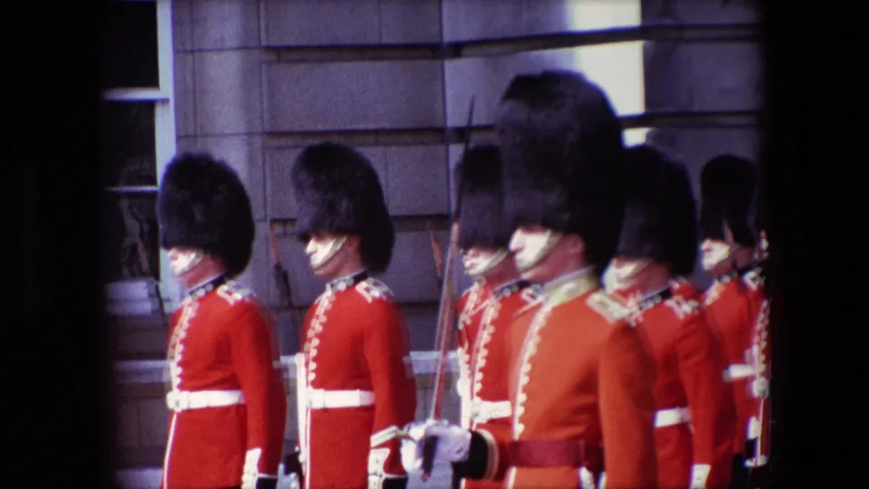 1967 London home-movie still with several ceremonial guards in red tunics and tall black hats standing close together, with rifles and white belts visible.