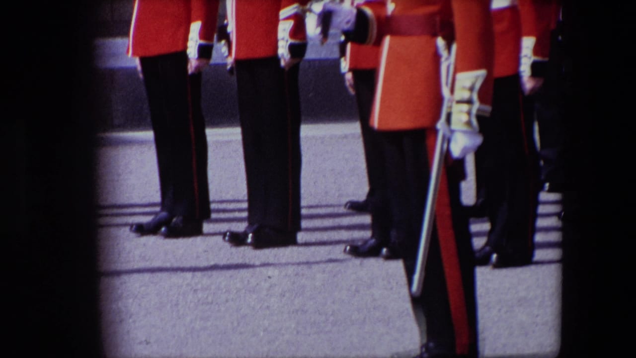Lower bodies of guards in red tunics and dark trousers stand on pavement.