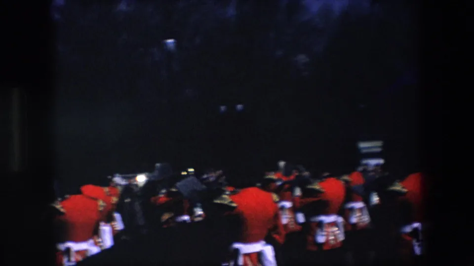 A handheld 1967 London view shows guards in red uniforms and drums moving away through a dark, tree-lined ceremonial route.