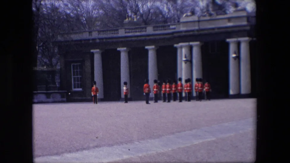 The final frame shows red-coated ceremonial guards arranged in formation across a paved London forecourt, with tall columns and winter-bare trees in the background.