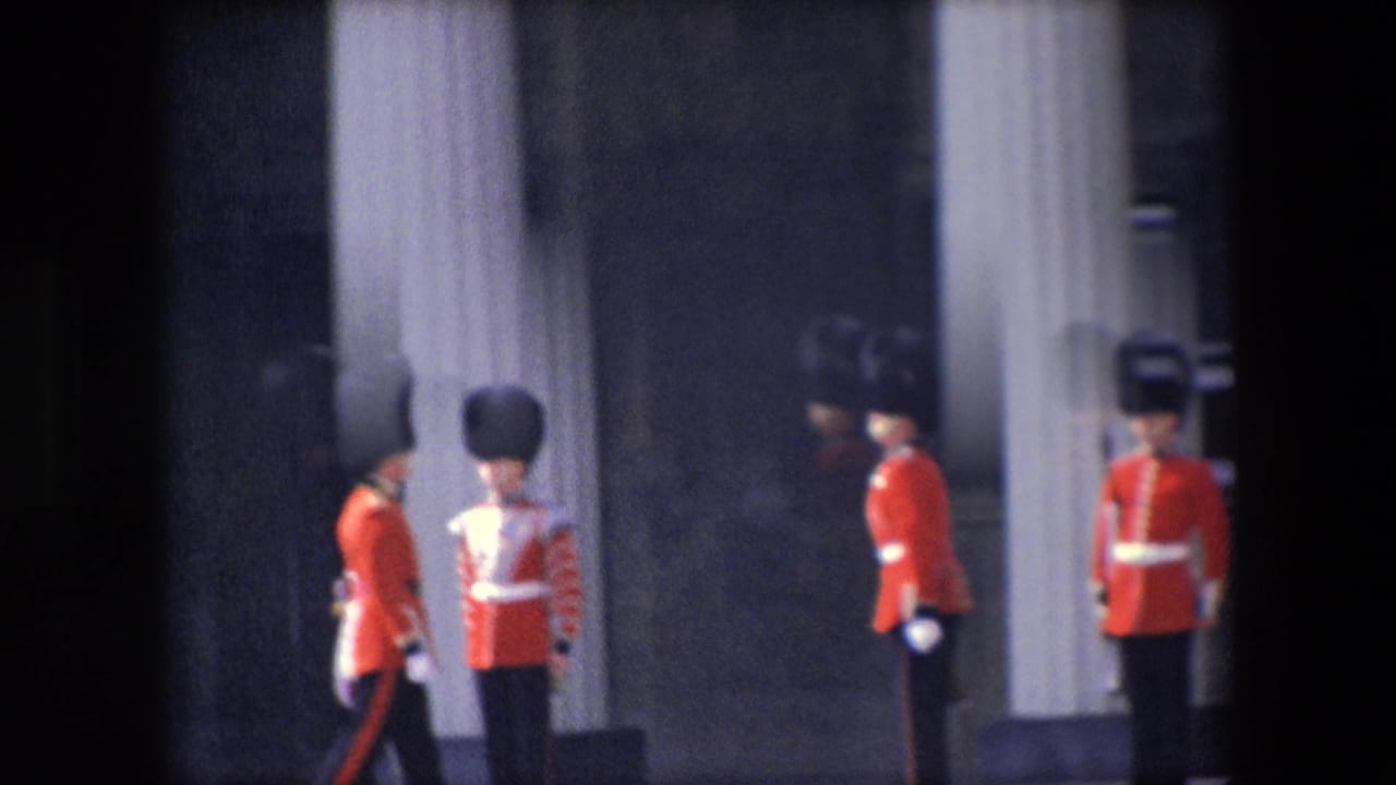1967 London home-movie frame showing red-uniformed British ceremonial guards with tall black hats near palace columns and dark entryways.