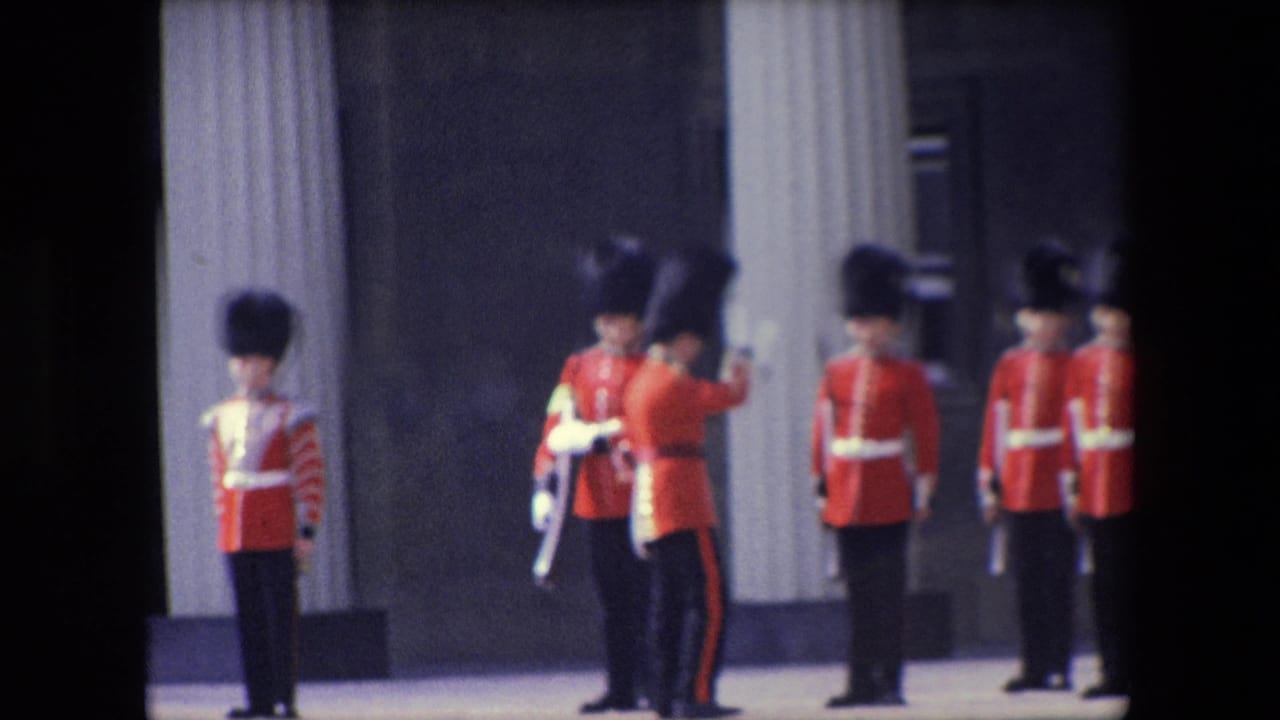 1967 London home-movie frame showing Queen's Guard soldiers in red ceremonial uniforms and tall black caps standing near pale columns while another guard faces the formation.