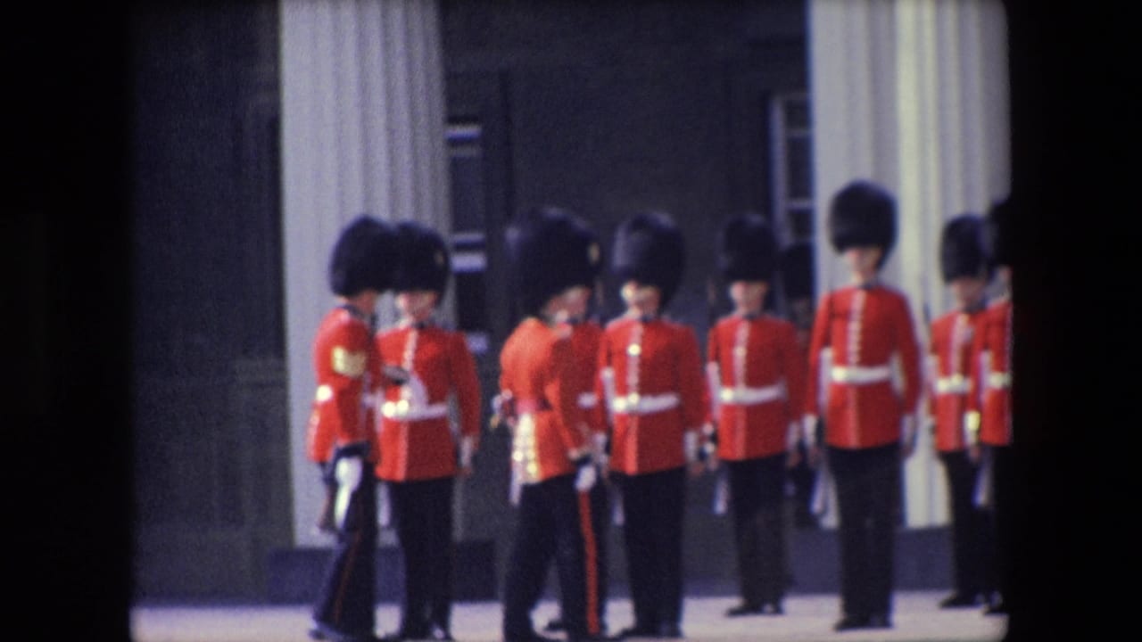 1967 London home-movie frame showing ceremonial British guards in red tunics and tall dark hats standing in formation beside pale columns.