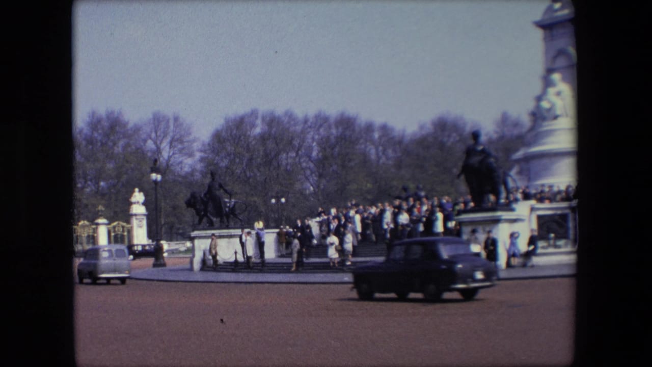 Dark car moves across a road with a crowd and large monument in the background.