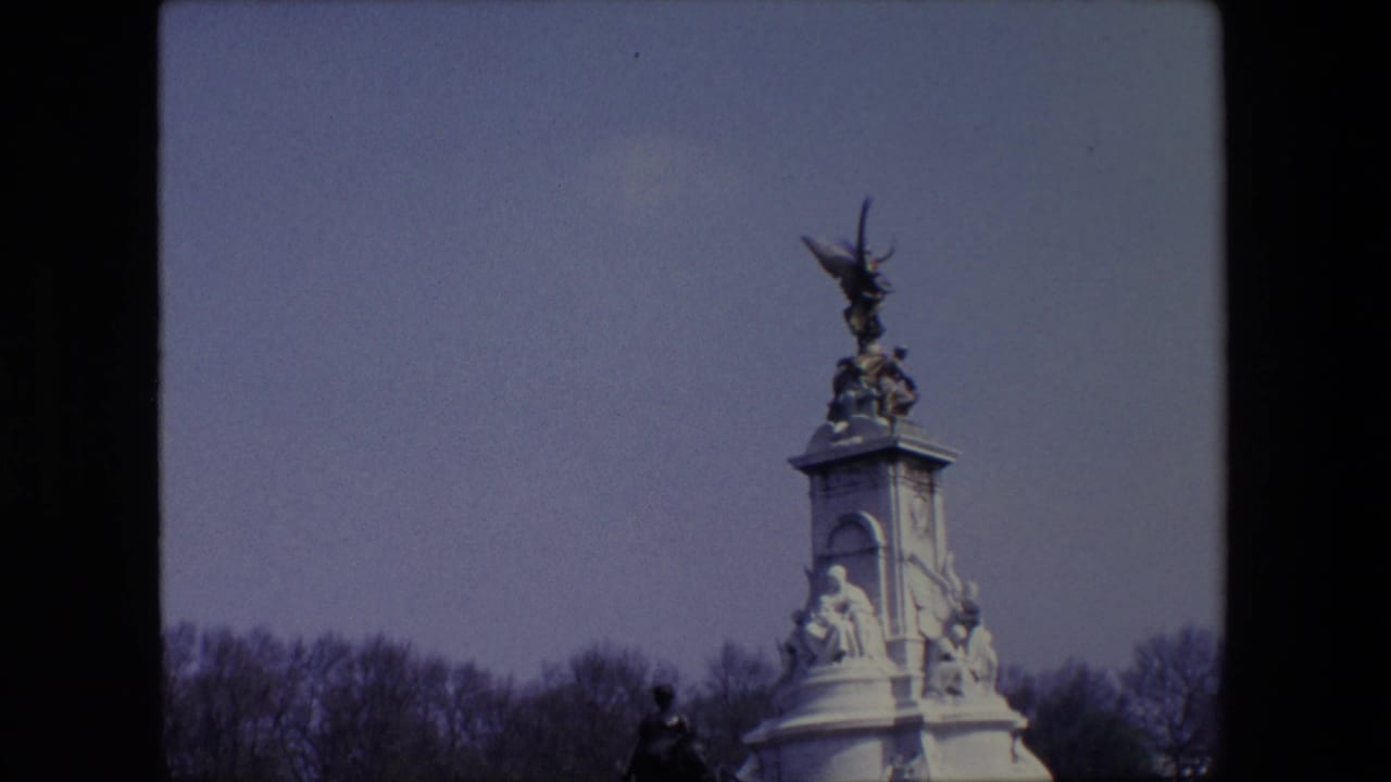 Upper portion of a tall monument against blue sky with bare trees behind it.