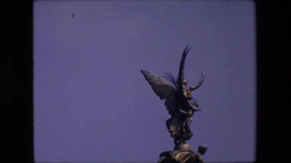 Final 1967 London frame holds on the winged statue and sculptural base above the stone pillar, with the subject low in the frame and open sky behind.