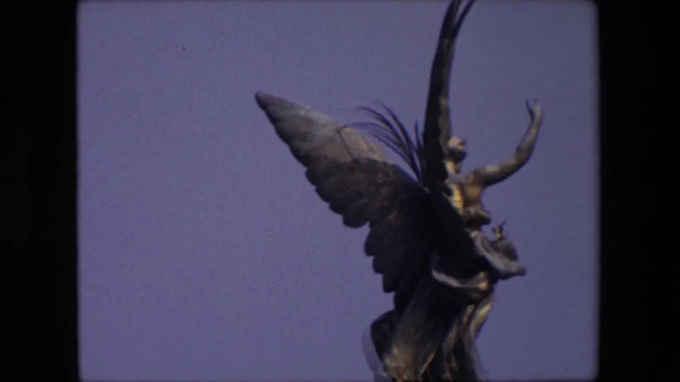 A closer 1967 London frame shows the winged figure’s feathered wing, raised arm, and draped form against open sky.
