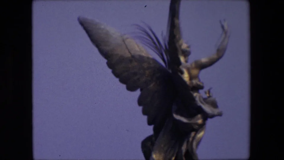 A soft 8mm close view from London in 1967 emphasizes the statue’s wing, upper body, and raised arm against a pale blue sky.