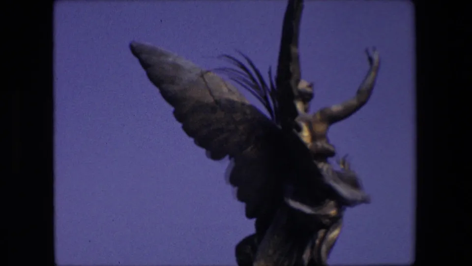 The final 1967 London frame holds on the winged statue in soft focus, showing the raised arm, feathered wing, and draped lower shape.