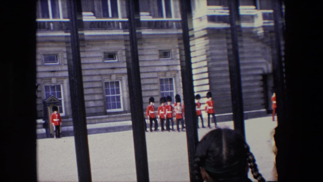 A group of guards gathers near the palace wall as foreground spectators are silhouetted behind railings.