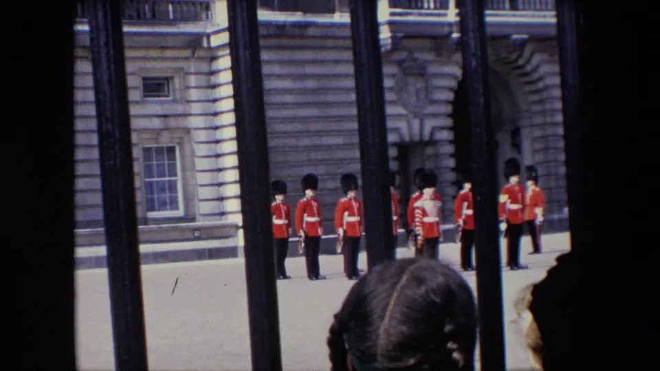 1967 London frame of red-coated British guards standing at a ceremonial post behind iron railings, with spectators partly visible at the lower edge.