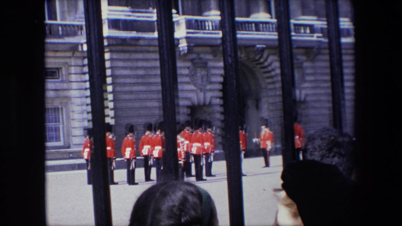 A group of Royal Guards stands near a stone entrance as tourists watch from behind railings.