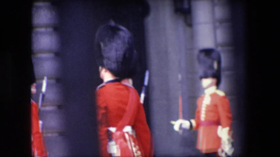 A close, partly obstructed 1967 London view shows red-uniformed guards with tall dark hats and white gloves outside a stone building.
