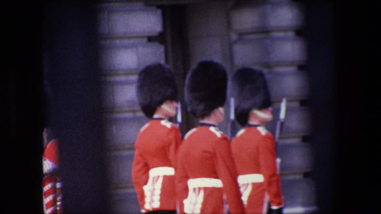Three red-coated guards are seen from behind beside a stone wall.