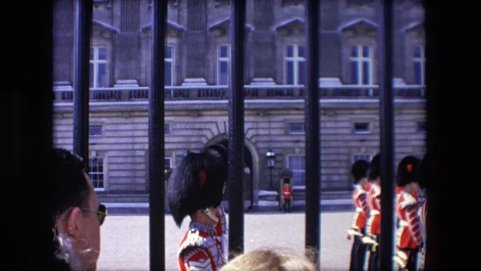 1967 London visitor-shot frame with spectators in the foreground, ceremonial guards beyond the railings, and a formal stone building facade across the courtyard.