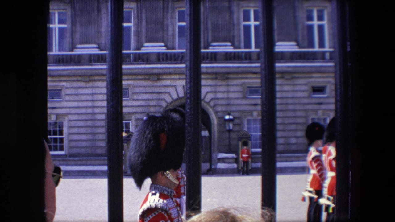 1967 London home-movie frame showing red-uniformed guards and sentry boxes viewed through black railings outside 10 Downing Street.