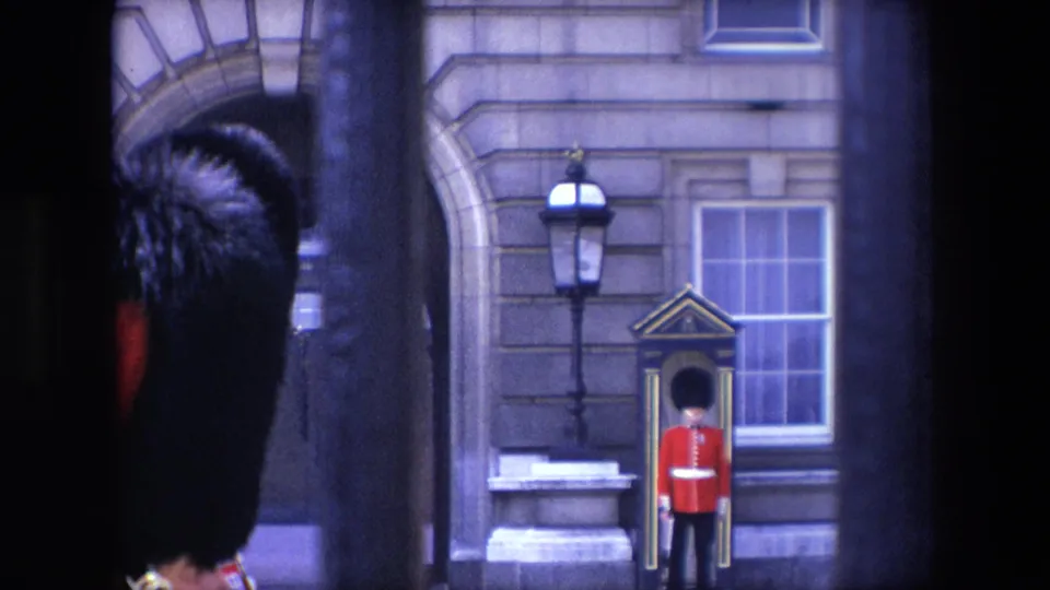 1967 London frame showing a red-coated guard standing near a sentry box outside 10 Downing Street, with dark railings and a close foreground guard shape.