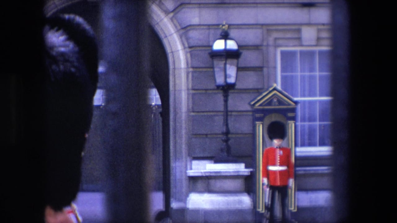 1967 London home-movie frame showing a red-uniformed Royal Guard at a sentry box, partly obscured by dark foreground shapes, with stone architecture and lamp posts behind him.