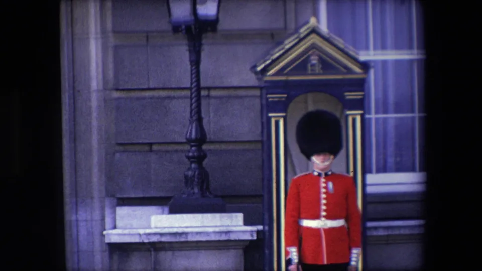 1967 London frame showing a ceremonial guard in red uniform beneath a striped sentry box canopy, filmed with visible 8mm borders and soft color.