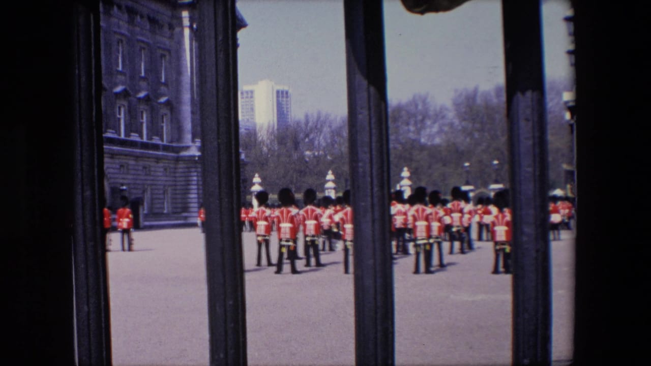 Royal Guard soldiers standing in formation behind dark gate bars on a paved forecourt.