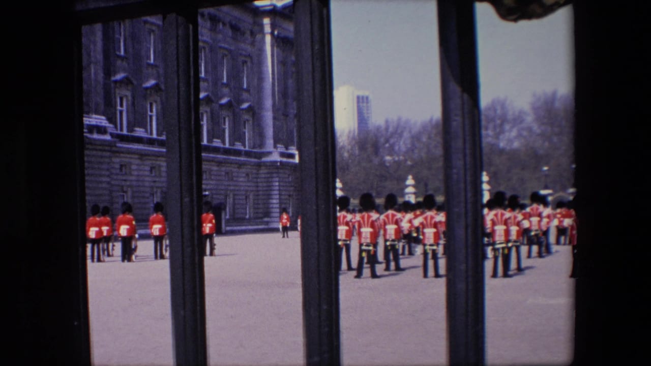 Guards in red uniforms stand in grouped formation near a large stone building.