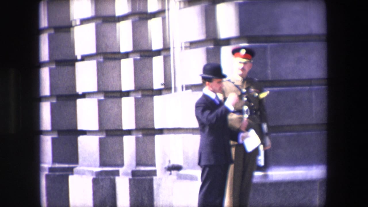 Suited man beside a uniformed officer near a stone building exterior.