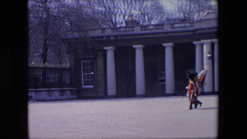 The guards remain in step while passing a columned exterior and railings, filmed from a steady visitor distance in 1967 London.