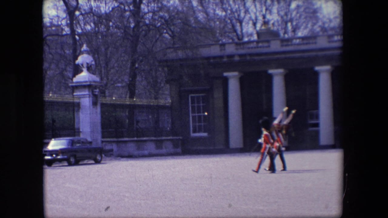 Uniformed guards crossing an open forecourt near a columned building and railings.