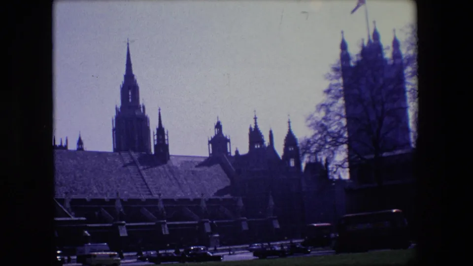 A dark silhouetted view of Gothic architecture and tower forms overlooks a London street with period cars and a bus at the bottom of the frame.