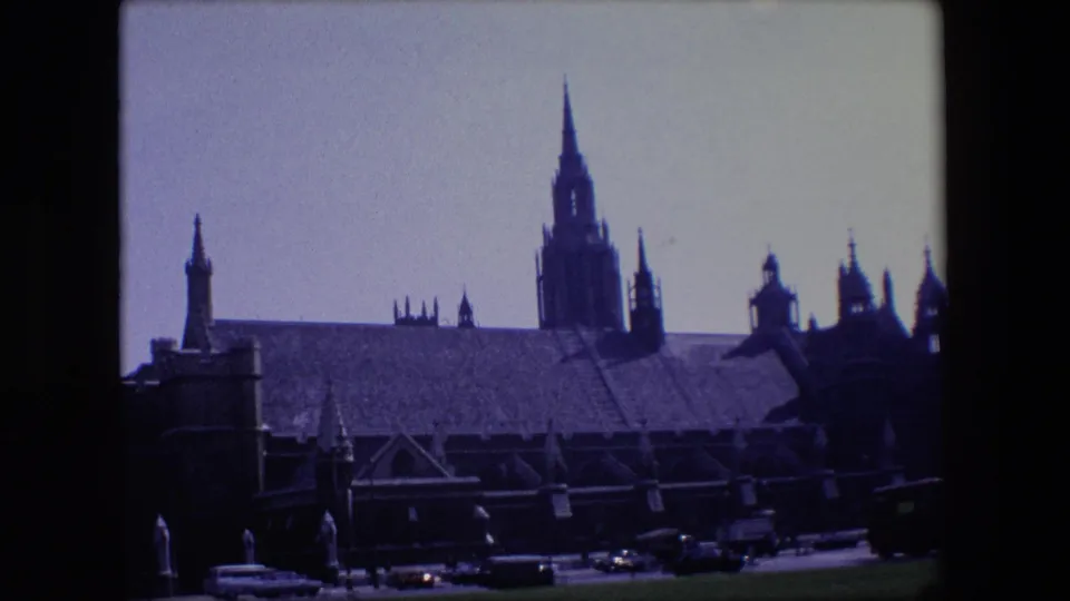 1967 London 8mm frame with a large spired building across the road, period vehicles, and dark foreground framing from the film scan.