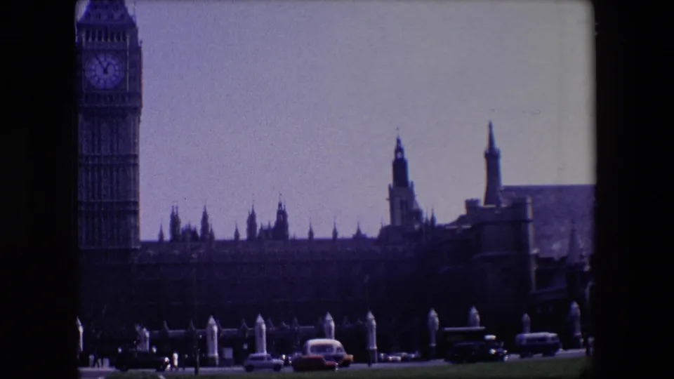1967 8mm view of Big Ben and the Palace of Westminster across a road with cars passing in the foreground.
