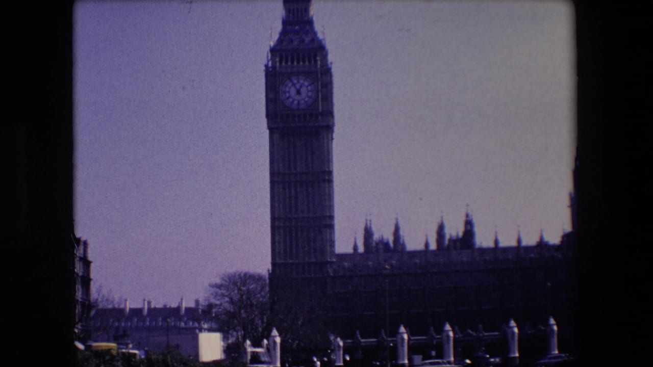 Big Ben and part of the Houses of Parliament seen across a street under a pale sky.