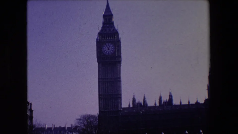 1967 London home-movie frame with Big Ben and the adjoining parliamentary building silhouetted against a clear pale sky.