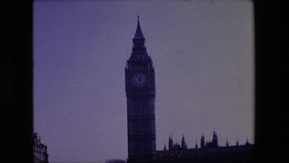1967 London 8mm view of Big Ben with adjacent roof spires, partial street buildings, and visible film gate edges.