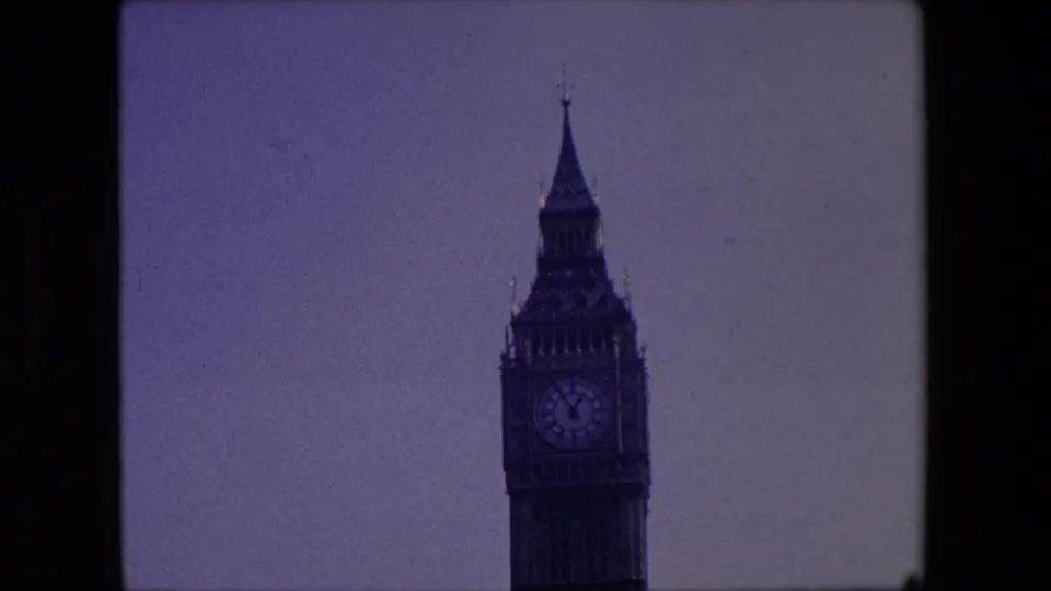 1967 London frame with a closer view of the Elizabeth Tower clock face, spire, and upper masonry, recorded with grainy 8mm home-movie texture.