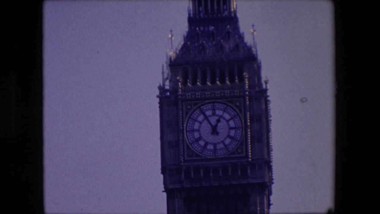 Distant view of the Westminster clock tower clock face against pale sky.