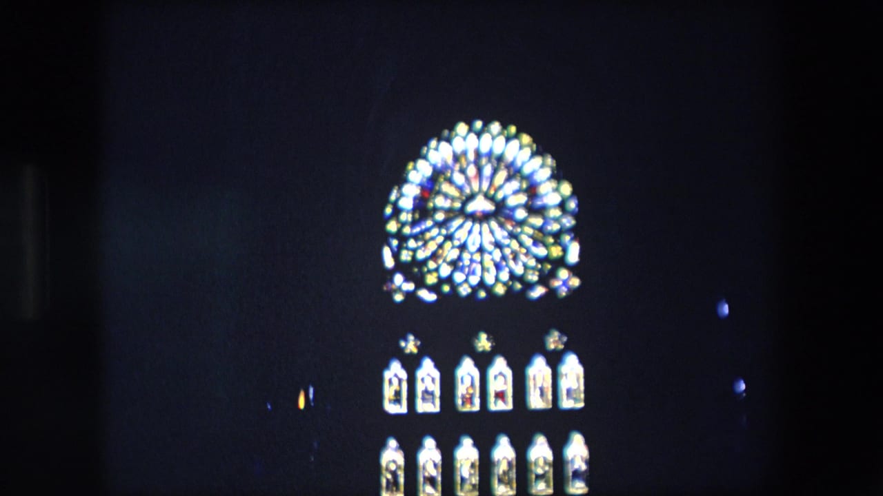 Small bright stained-glass church window against a dark interior.