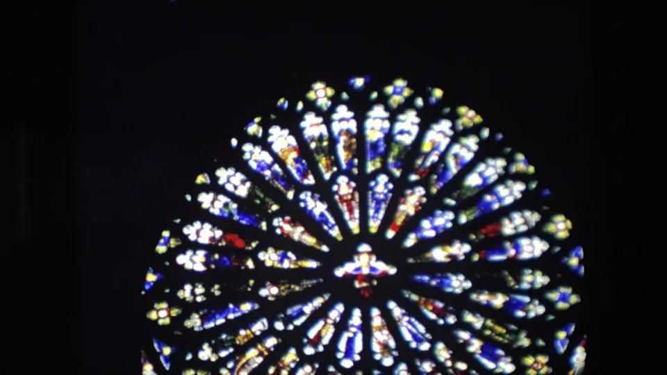 Final close-up frame of the London church stained-glass window, dominated by a bright circular rose pattern set against a nearly black interior.