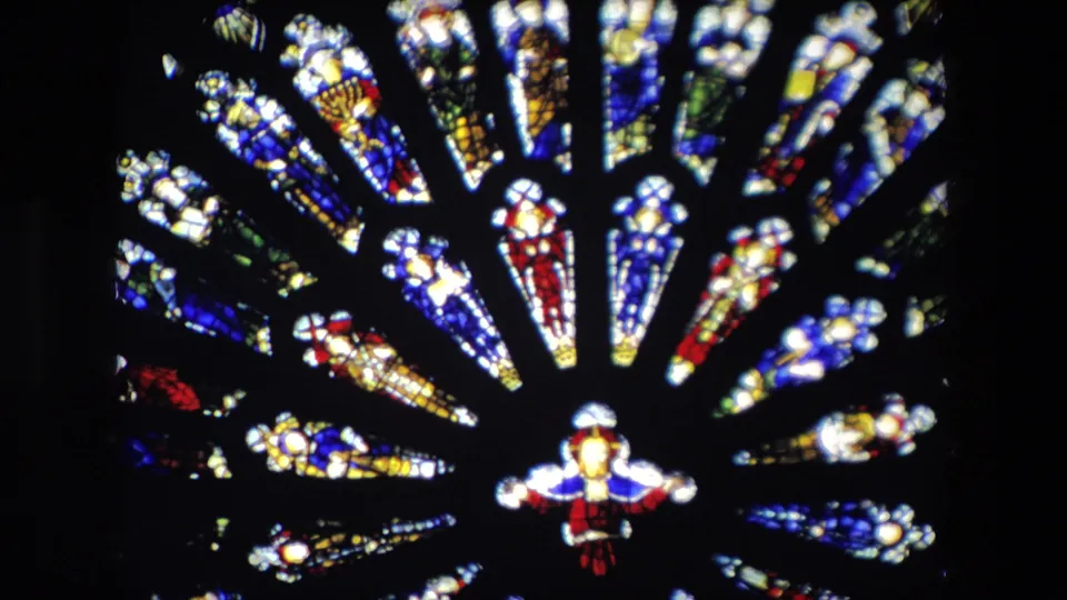 Closer view of a stained glass window in the supplied London church clip, showing bright blue, red, yellow, and white panes around a small human figure in the glass.