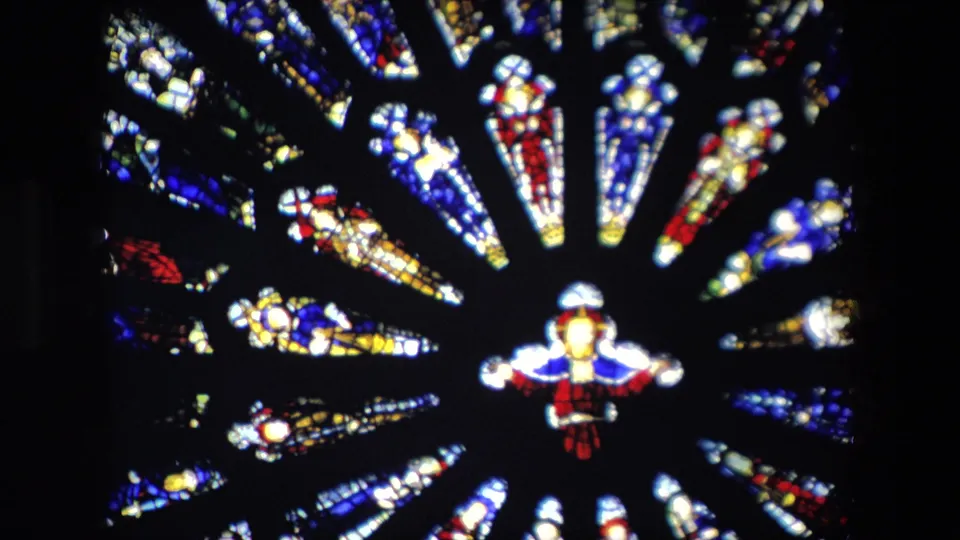 1967 London home-movie frame showing a close, slightly soft view of a circular stained glass window with red, blue, yellow, and white glass around a central figure-like motif.