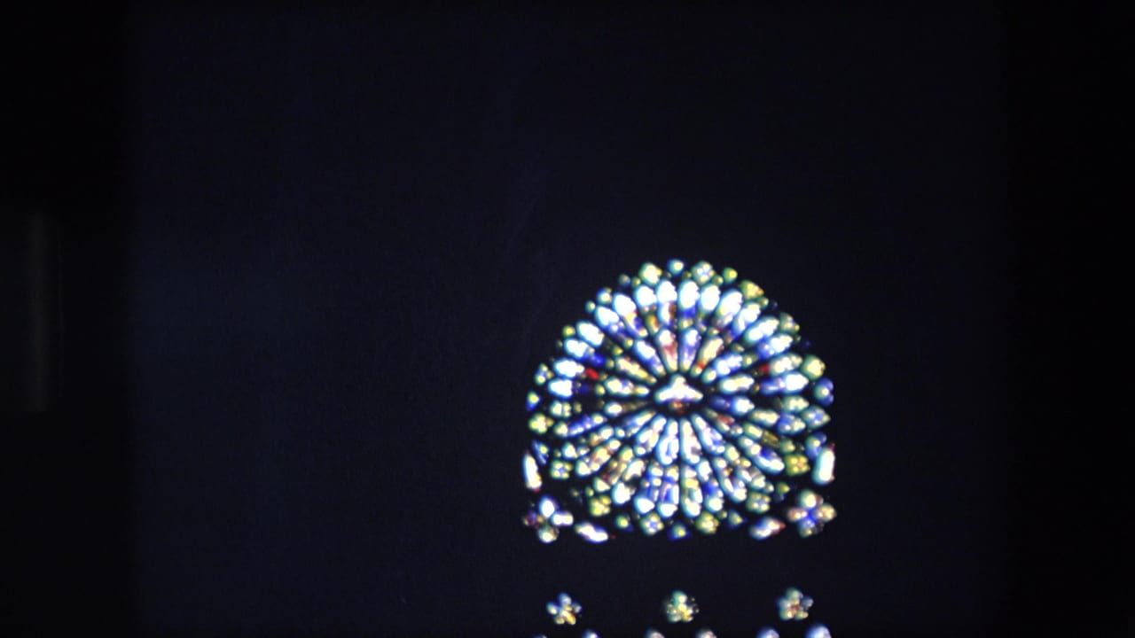 Smaller bright stained-glass window seen above a dark horizontal obstruction.