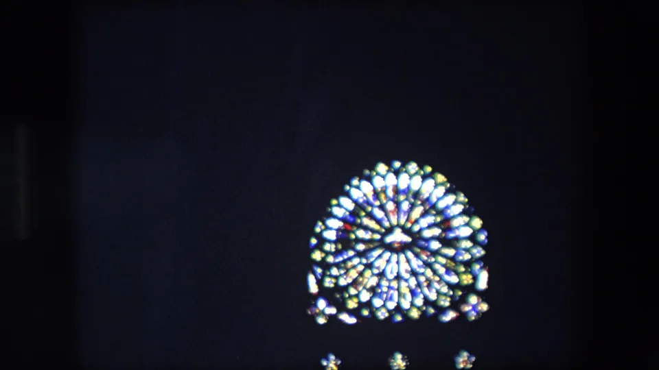 1967 London 8mm frame showing a bright circular stained-glass window above small points of light, with most of the interior held in shadow.