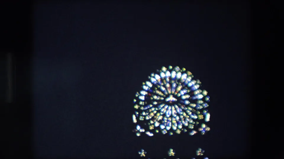 1967 London 8mm frame with a centered illuminated stained-glass window, possible religious motif, and small light points below in a dark interior.