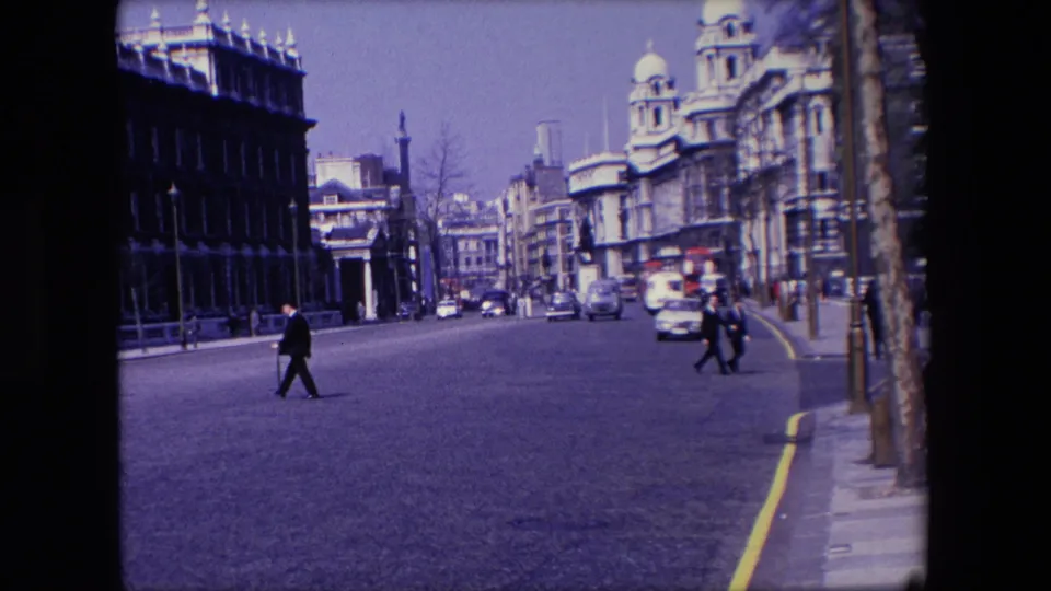 In the final 1967 London frame, pedestrians move across the roadway as cars pass near stone buildings, pavements, trees, and a distant vertical structure.