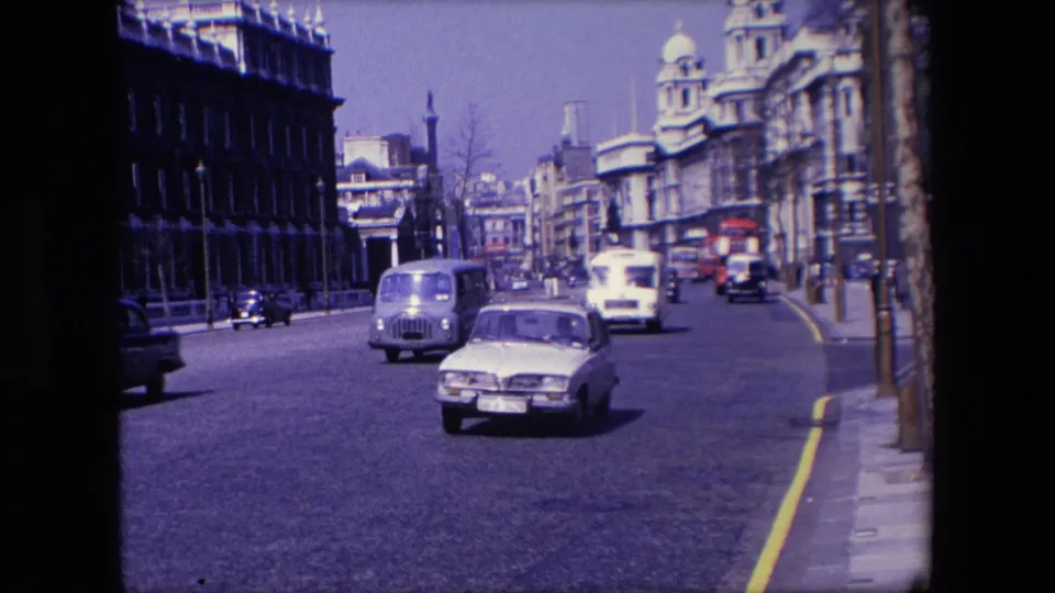 1967 London frame showing a white car in the foreground, a light commercial vehicle, other traffic, pedestrians, and dense urban architecture.