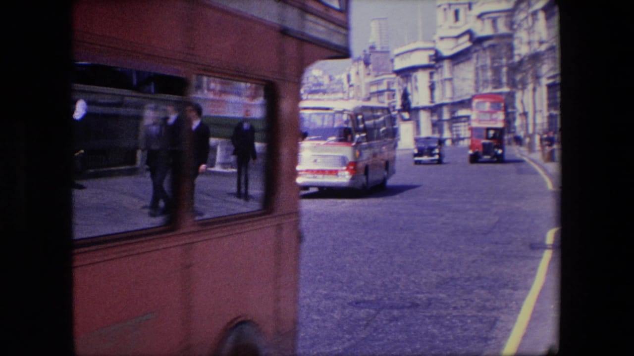 Red bus edge passing beside a London street with cars and buildings ahead.