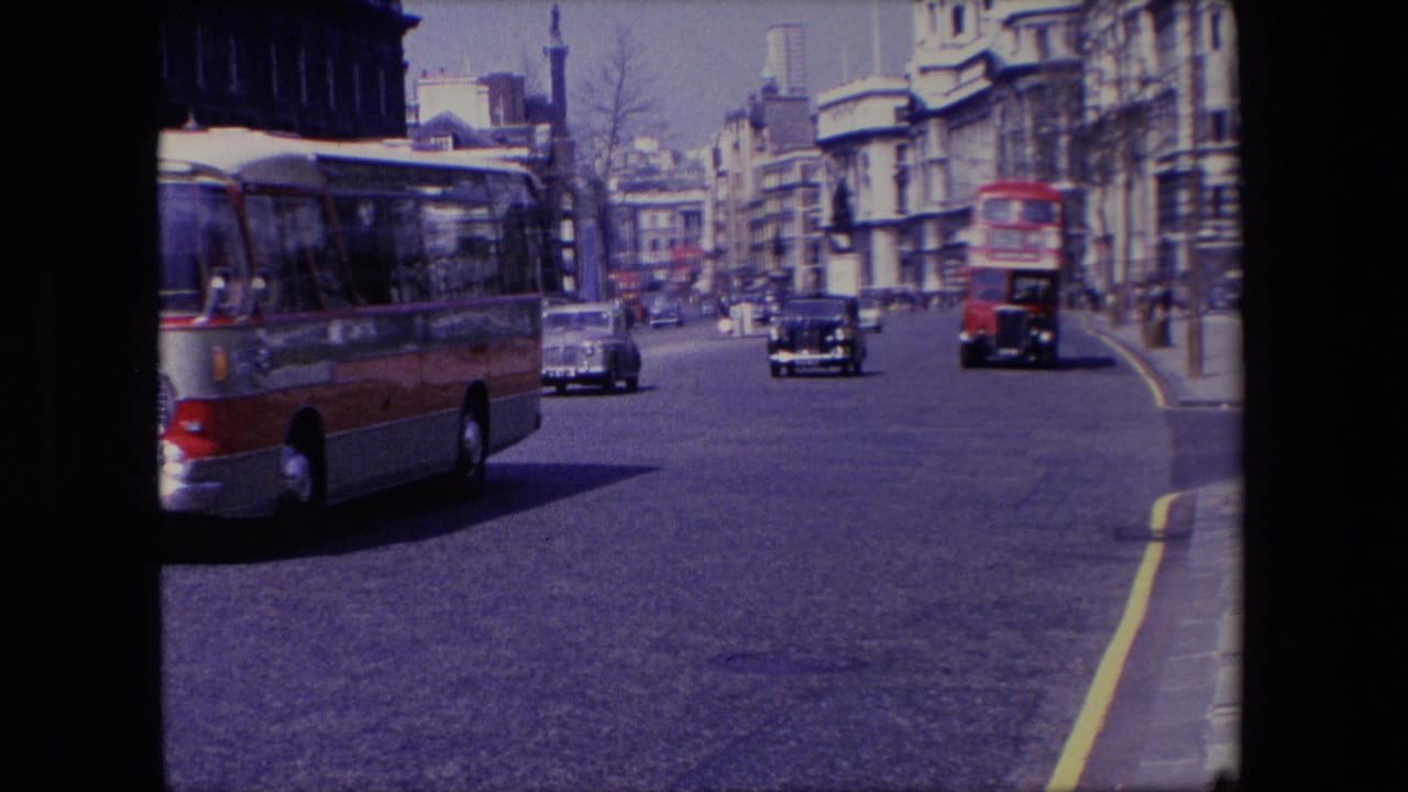 Red and gray bus passes through a broad street with cars and buildings beyond.