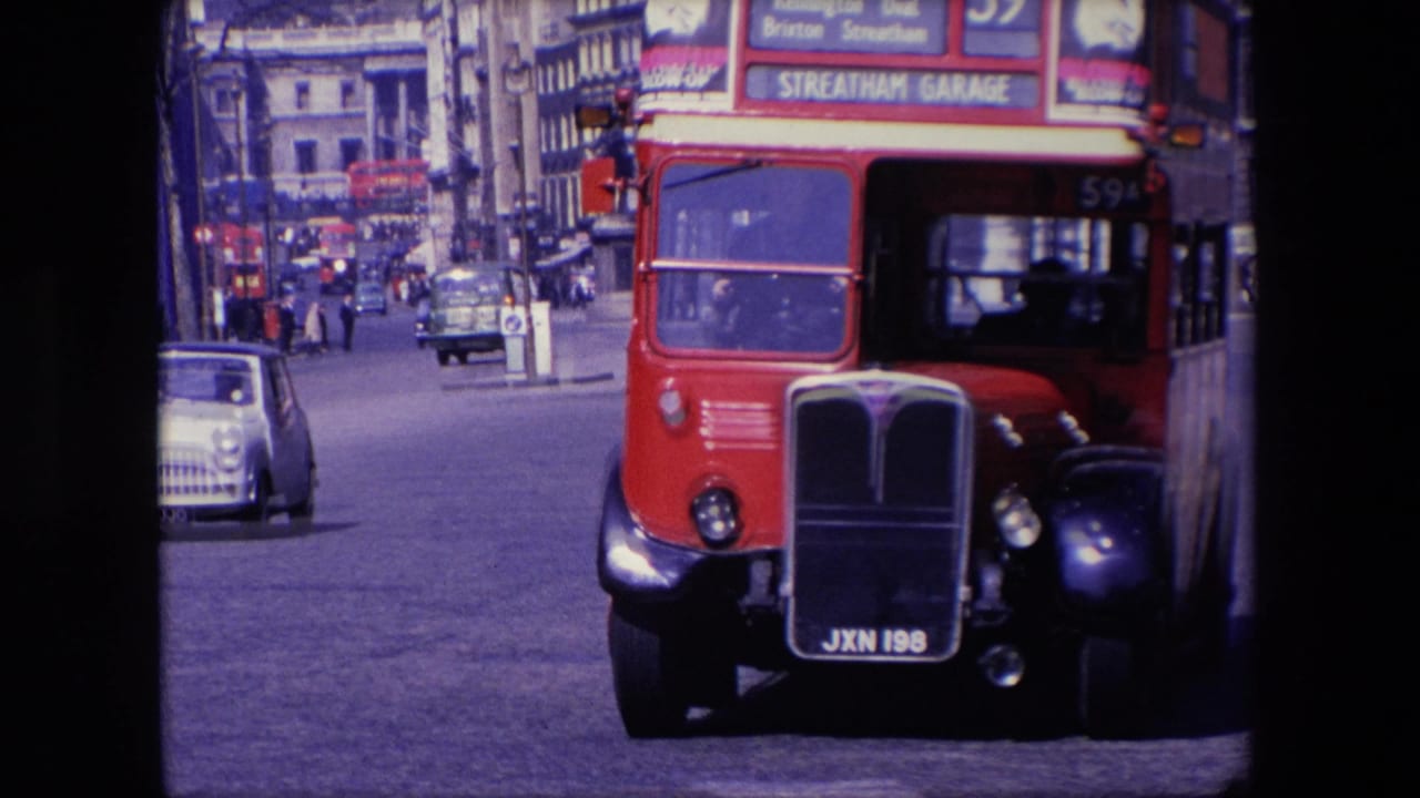 Red double-decker bus and black car pass through a busy London street.